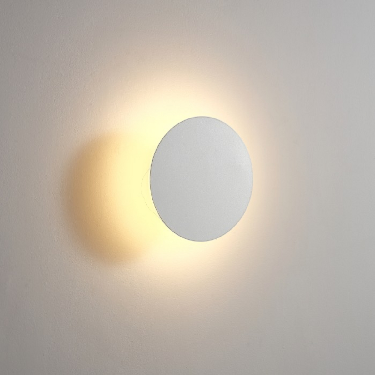 Ultra Beam Lighting Ltd round white LED bathroom wall sconce creating a warm halo light effect on a wall.