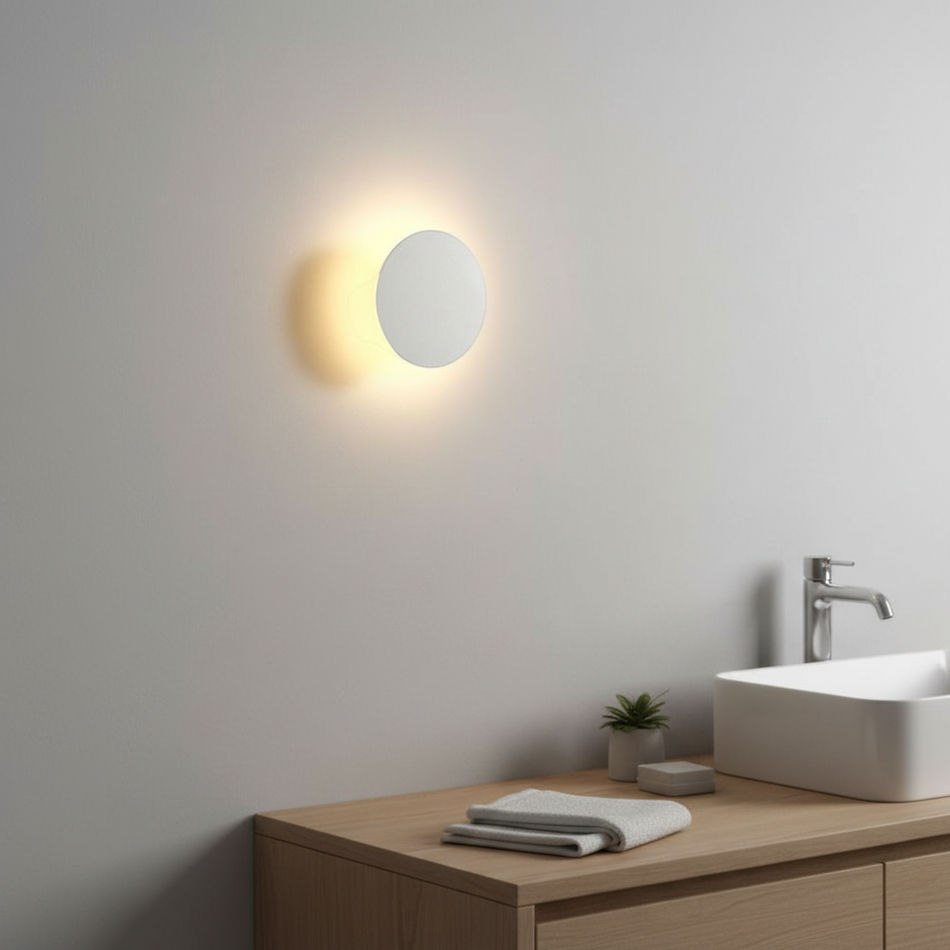 Ultra Beam Lighting Ltd round white LED bathroom wall sconce creating a warm halo effect on a grey wall.
