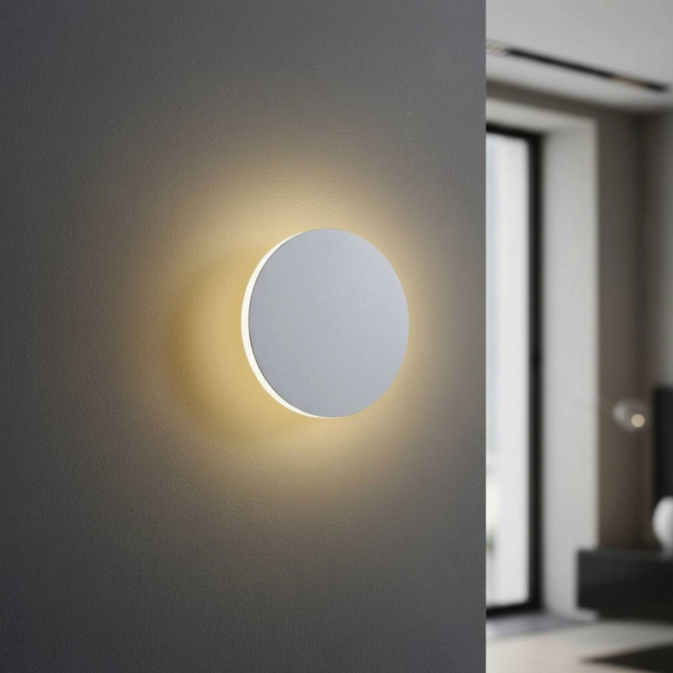 Ultra Beam Lighting Ltd round white LED wall light with acrylic diffuser creating a warm halo glow on a grey wall.