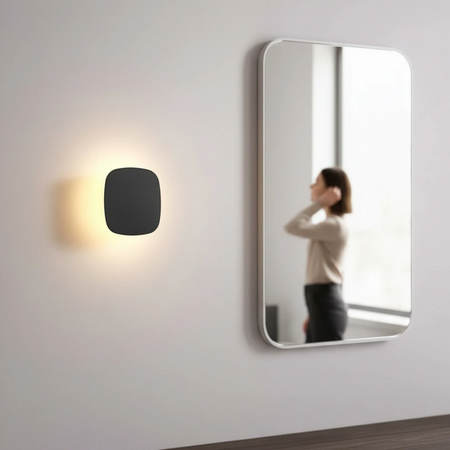 Ultra Beam Lighting Ltd square black LED vanity wall light with warm halo glow mounted next to a bathroom mirror.