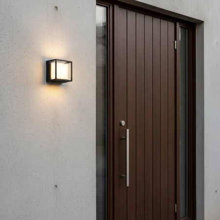 Ultra Beam Lighting Ltd 12W square black LED wall light mounted on a modern concrete exterior wall by a wooden door.