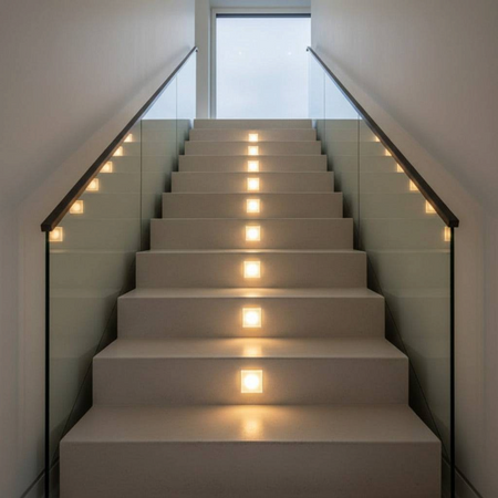 Ultra Beam Lighting Ltd square recessed LED stair lights installed in risers of a modern staircase with glass railing
