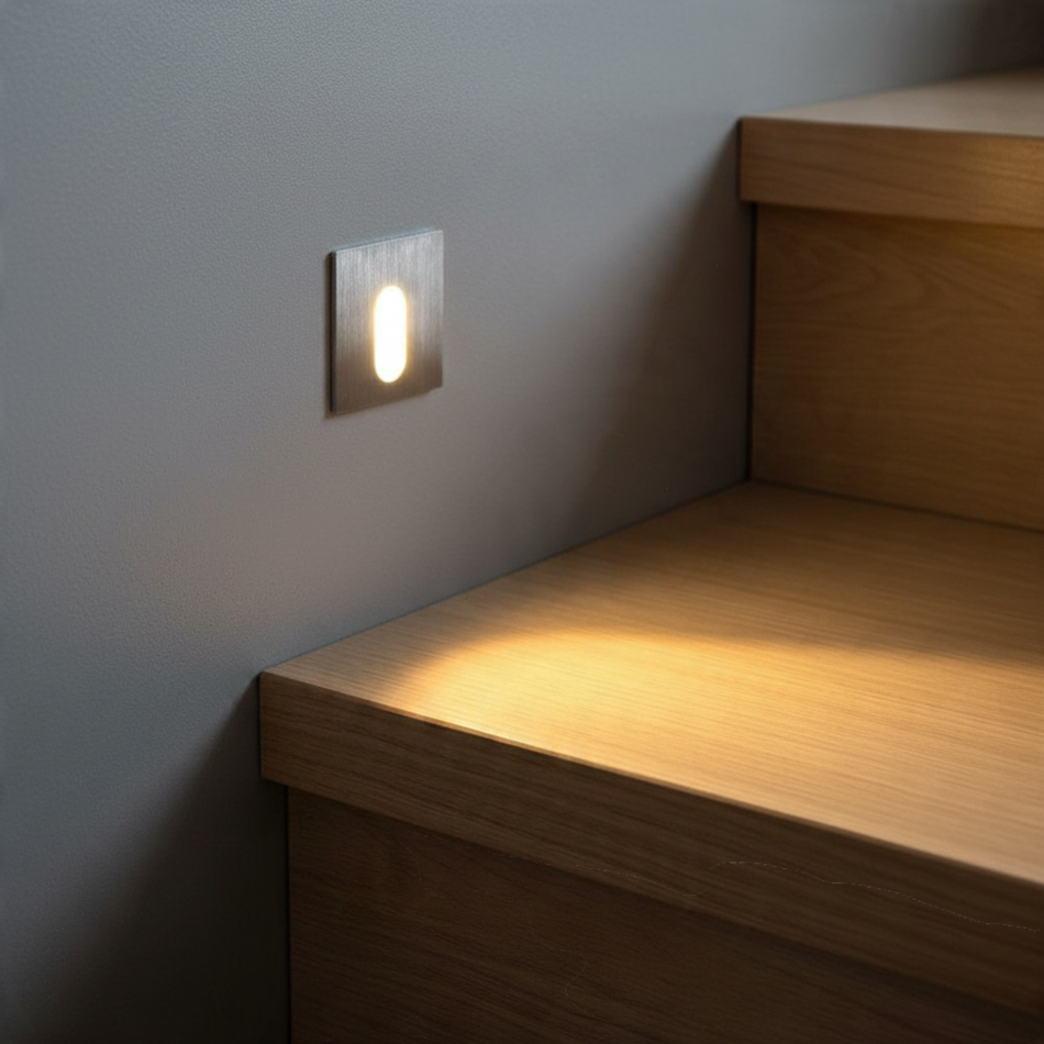 Ultra Beam Lighting Ltd square recessed LED stair light in brushed aluminum casting a warm glow on wooden steps