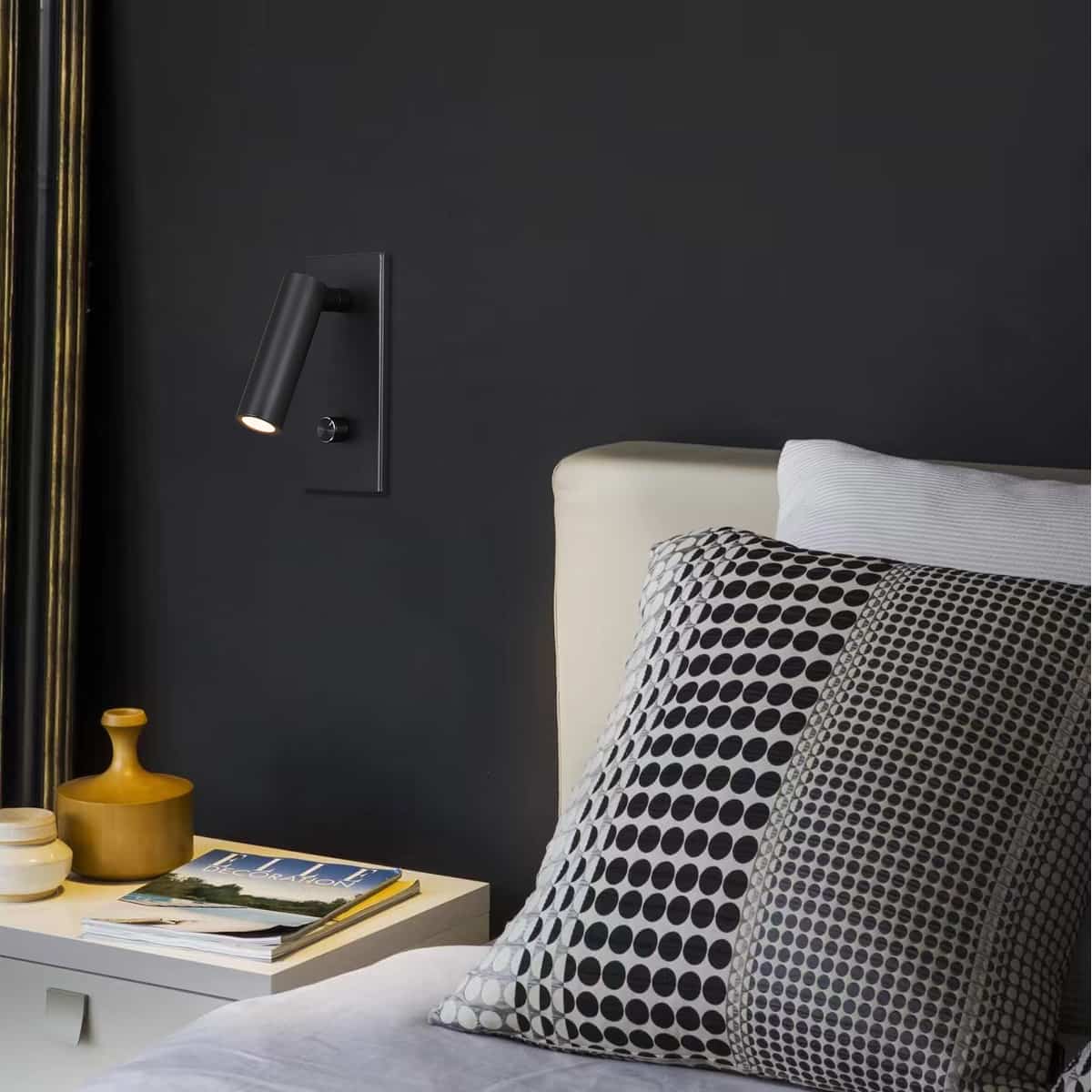 black dimmable reading light mounted on a black wall next to a bed